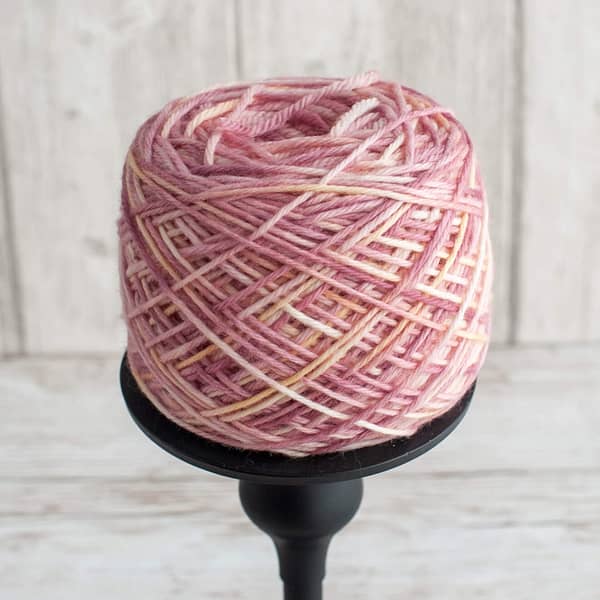 A pink and cream skein of yarn wound into a cake