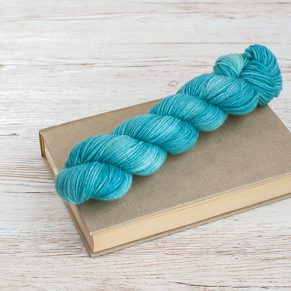 A pastel green-blue skein of yarn on top of a book