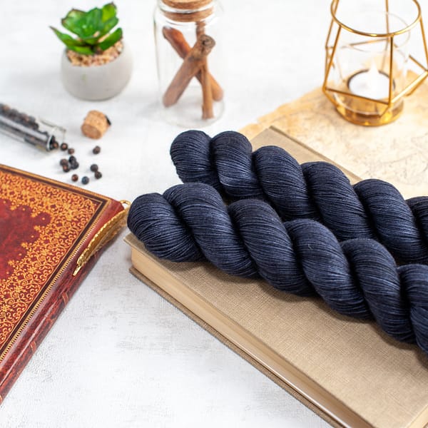 two skeins of fingering weight blue-black yarn laying on top of a book